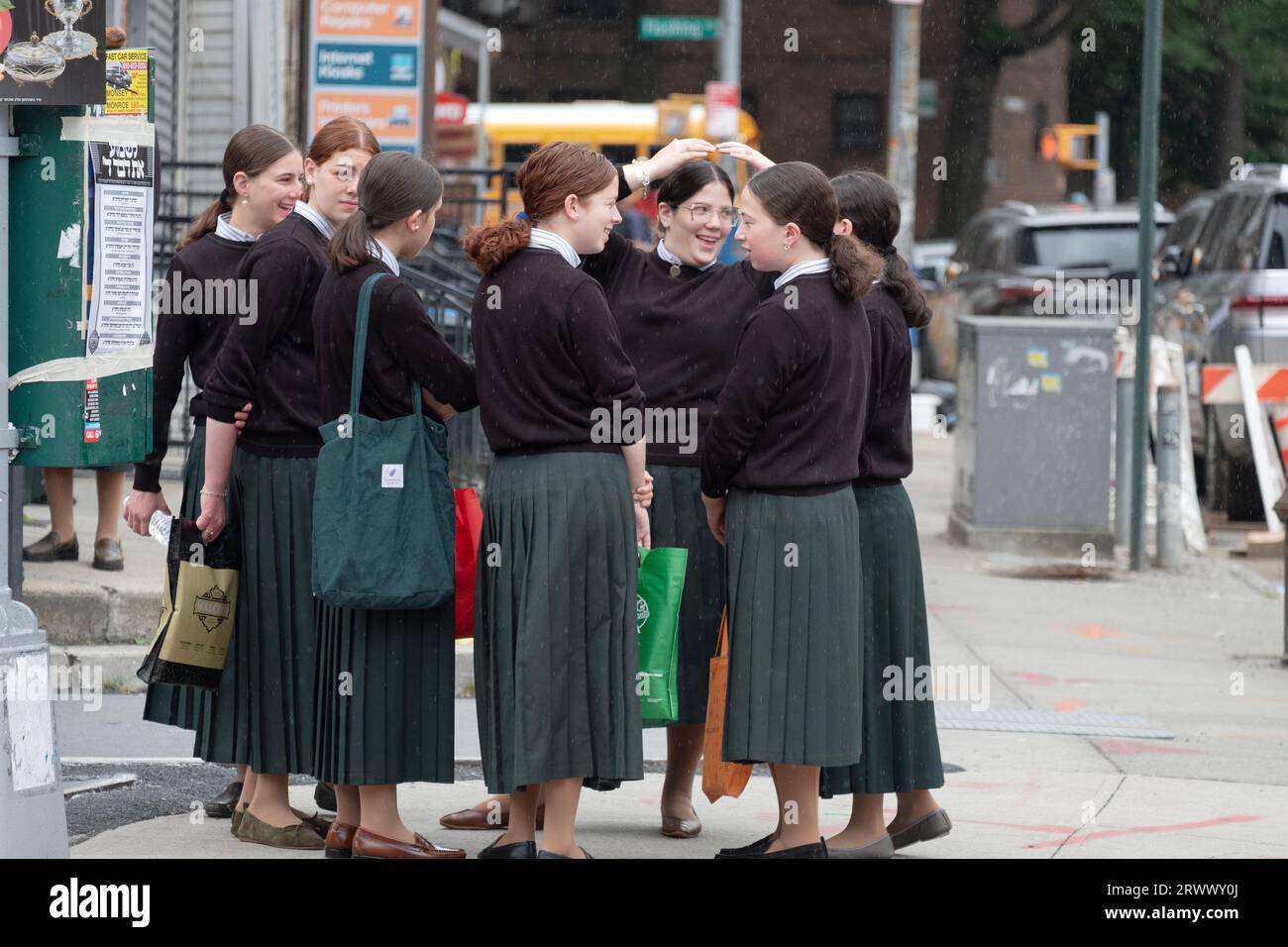 In einem leichten Nieselregen sitzen orthodoxe jüdische Mädchen, während sie auf einen Schulbus warten. An der Lee Avenue in Williamsburg, Brooklyn, New York. Stockfoto