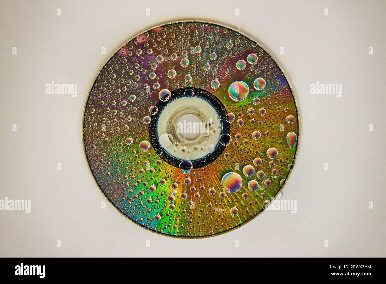 CD auf weißem Hintergrund mit Regenbogenwassertropfen auf reflektierender Metalloberfläche Stockfoto