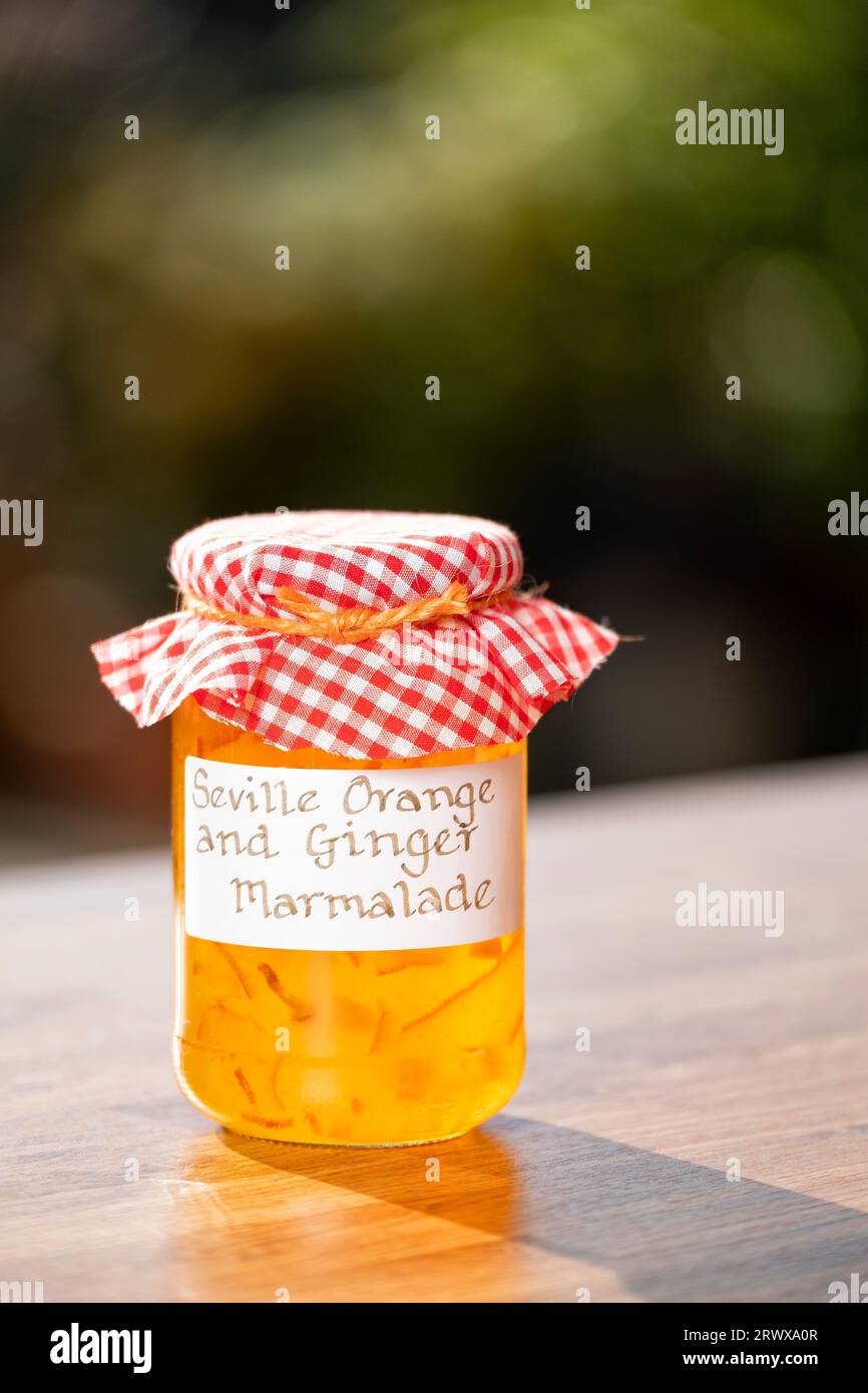 Ein Glas mit hausgemachter Sevilla Orange und Ingwermarmelade. Der Deckel des Behälters ist mit einem handgeschriebenen Etikett und Stoff versehen Stockfoto