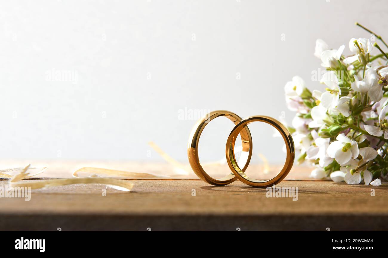 Detail von zwei goldenen Ringen auf einem rustikalen Holztisch mit Blumenstrauß und weißem isoliertem Hintergrund. Vorderansicht. Stockfoto