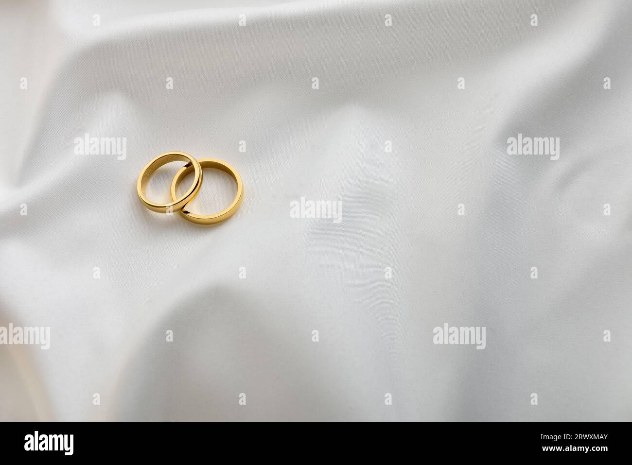 Zwei elegante Ringe aus Gold übereinander auf weißem, glänzendem Stoff. Draufsicht. Stockfoto