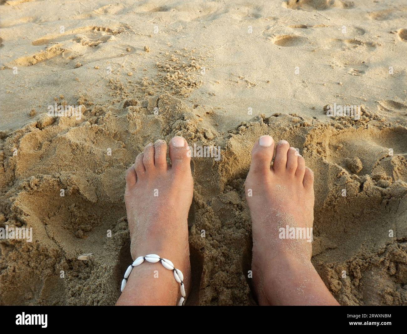 Die Füße eines Mannes auf dem Strand, der mit einem Knöchelarmband verziert ist Stockfoto