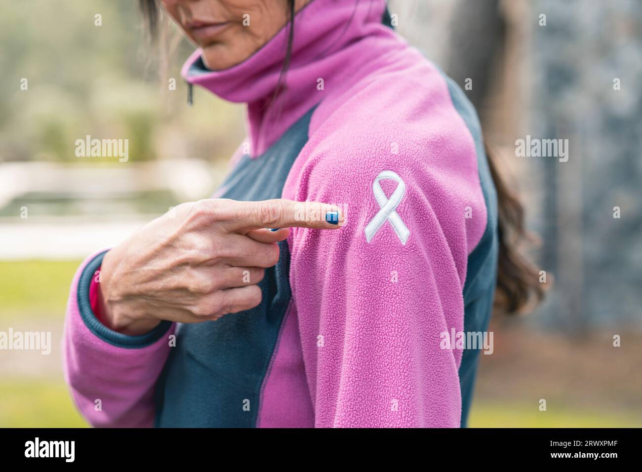 Frau, die auf ein gesticktes Krebsbewusstseinsband zeigt, mit dem Finger auf ihrem Sweatshirt Stockfoto