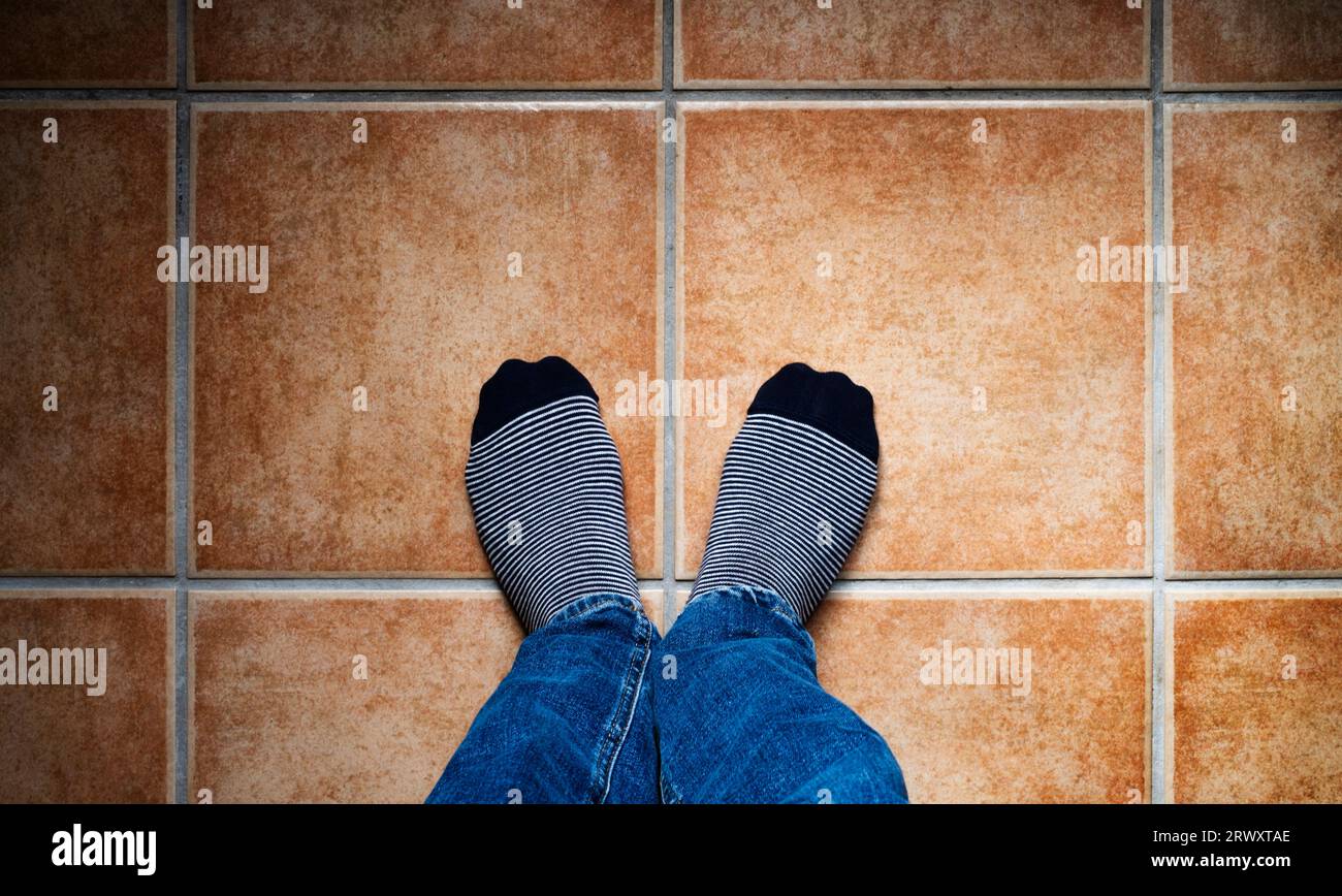 Bild von oben von zwei Füßen mit gestreiften Socken auf einem gefliesten Boden in warmen Tönen. Selfie-Konzept. Stockfoto