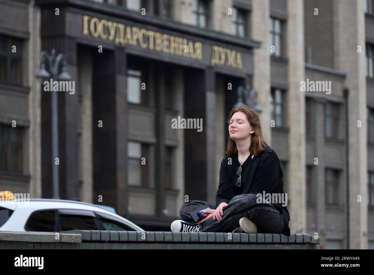 Mädchen, das mit geschlossenen Augen auf der Bank gegen die Staatsduma in Moskau sitzt Stockfoto