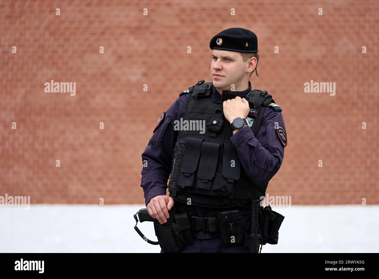 Russischer Polizeibeamter der Spezialkräfte in kugelsicherer Weste, der auf der Straße der Stadt auf Kreml-Hintergrund steht Stockfoto