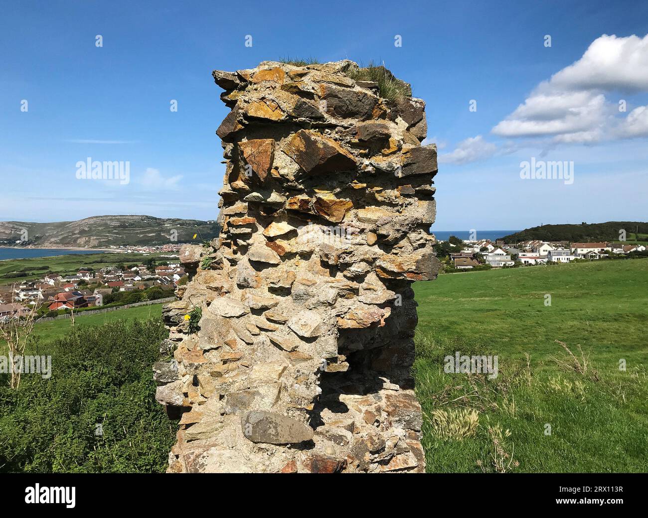 Blick auf die Ruinen des Eingangs von Deganwy Castle, Wales, die einen Felsen aus ordovizischem rhyolitischem Tuffstein überragen und in der Ferne in Richtung Llandudno blicken Stockfoto