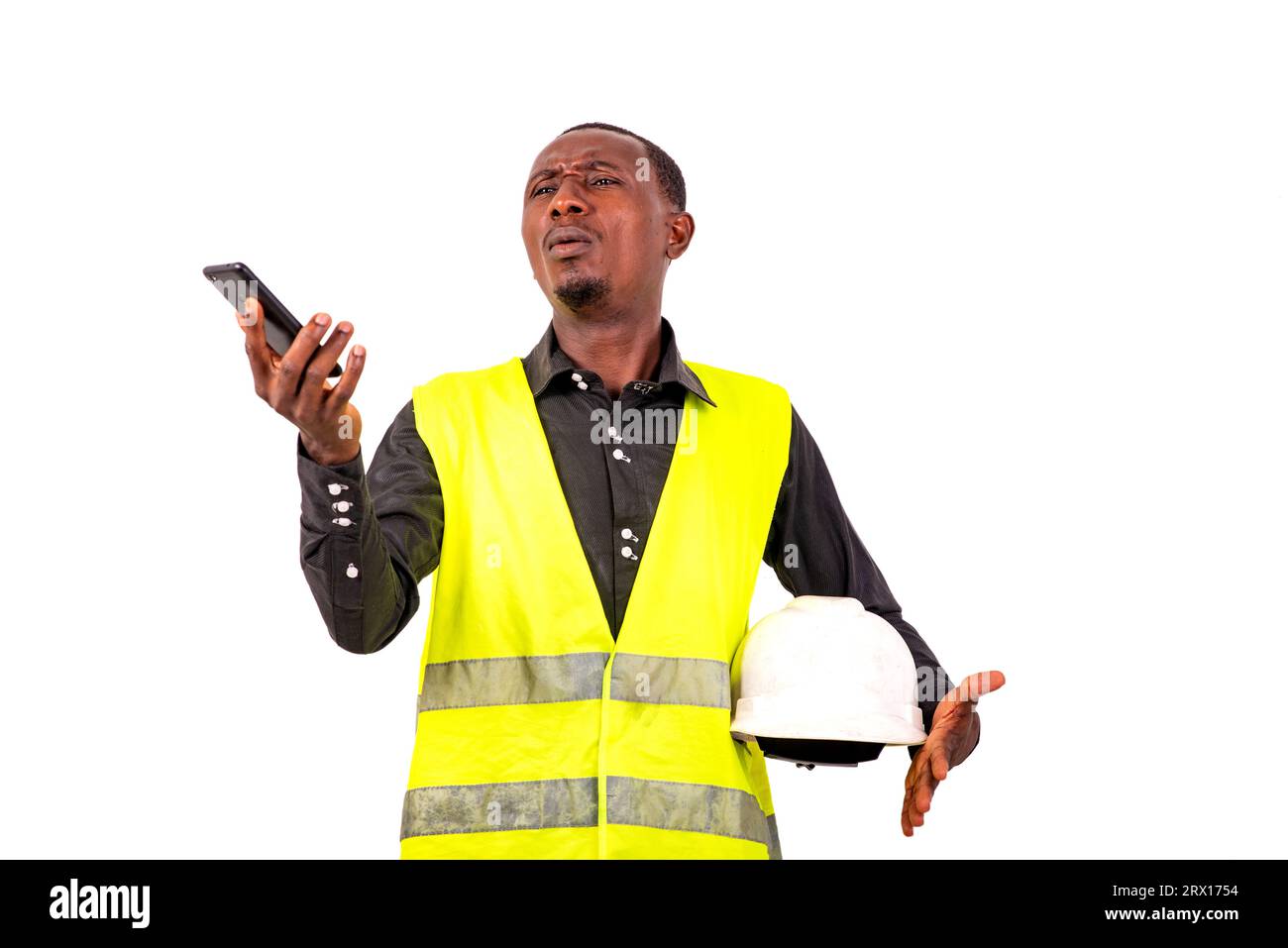 Junger Ingenieur trägt grüne Weste und Schutzhelm, während er das Handy hält. Stockfoto