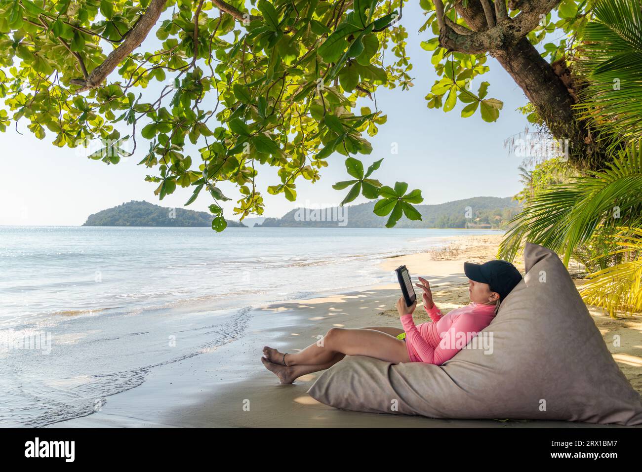 Digital Escape, eine entspannende Frau mit einem E-Book am Strand“ Stockfoto