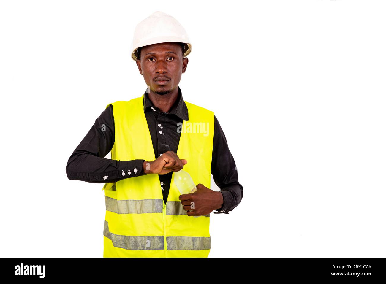 Junger Techniker mit grüner Weste und Schutzhelm, der die Mineralwasserflasche aus Kunststoff öffnet. Stockfoto