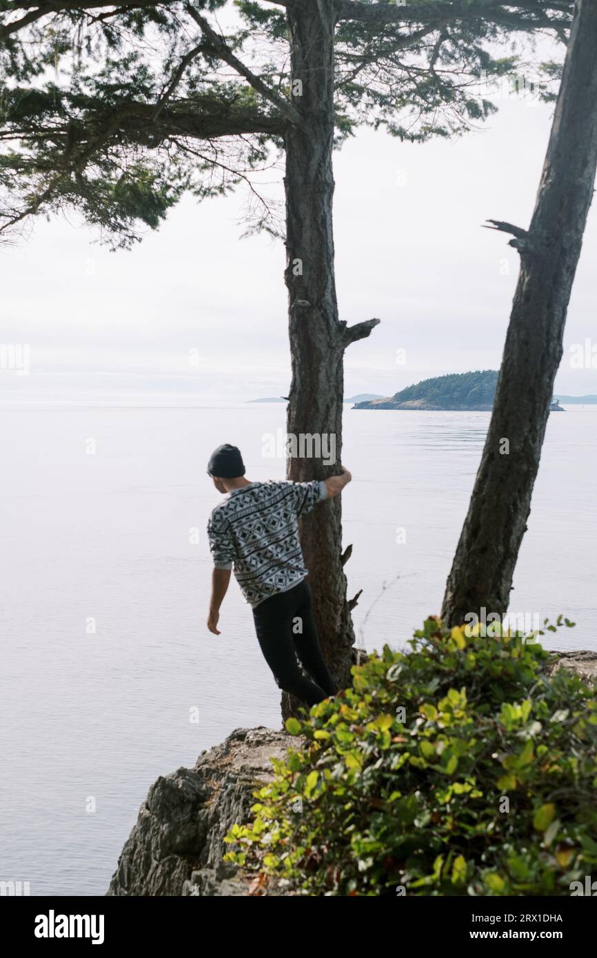 Mann in Beanie mit Blick auf das Meer von den Klippen Stockfoto