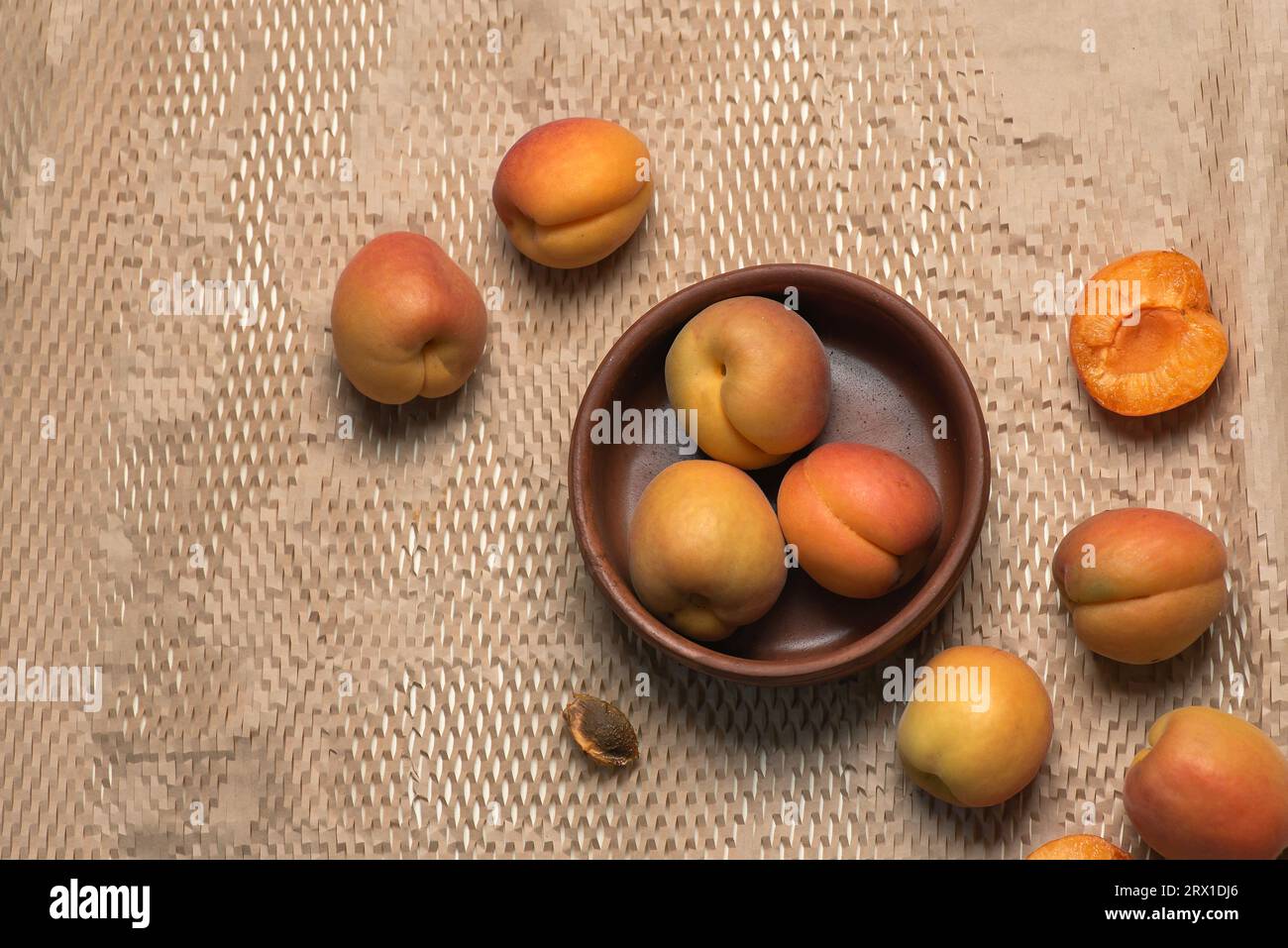 Frische, reife, saftige Aprikosen in einer braunen Schüssel auf hellem Hintergrund. Ganze Früchte, Früchte um die Schüssel, Aprikosenkerne Stockfoto