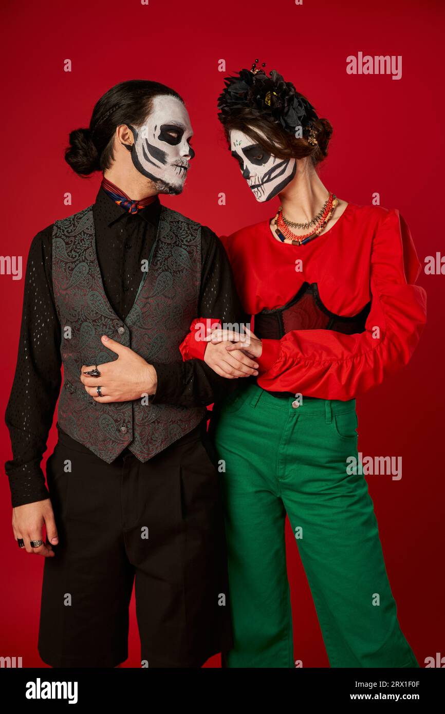 Ein Paar in trendiger Kleidung und Skelett-Make-up auf rot, DIA de los muertos Feier Stockfoto