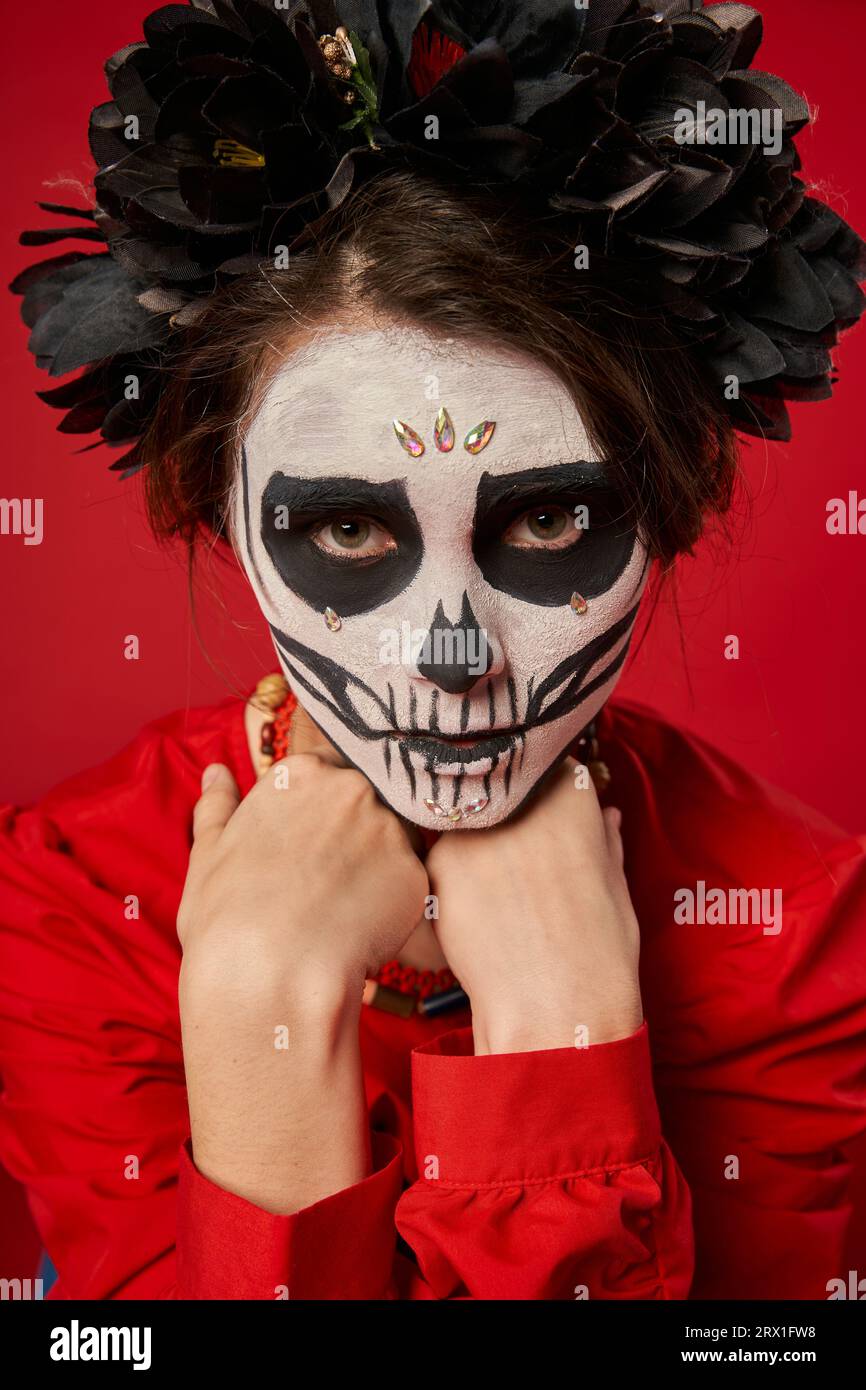 Frau mit gruseligen Schädelschminken und schwarzem Kranz, die Kamera auf rotem, DIA de los muertos-Konzept ansieht Stockfoto