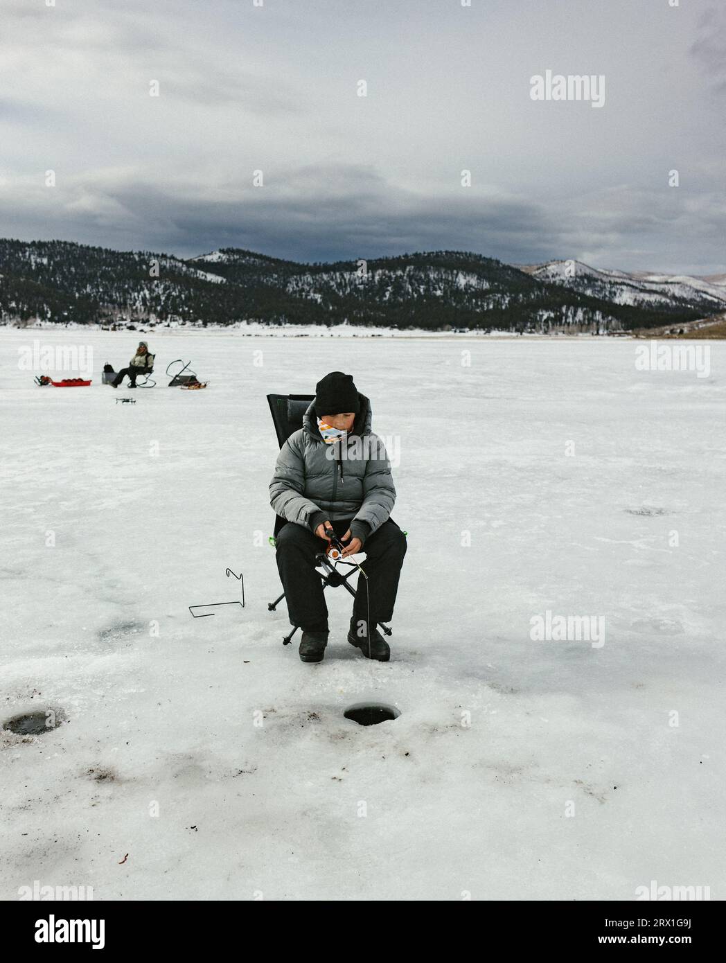 Teenager-Jungs sitzen auf gefrorenem See in den Bergen, Eisfischen draußen Stockfoto