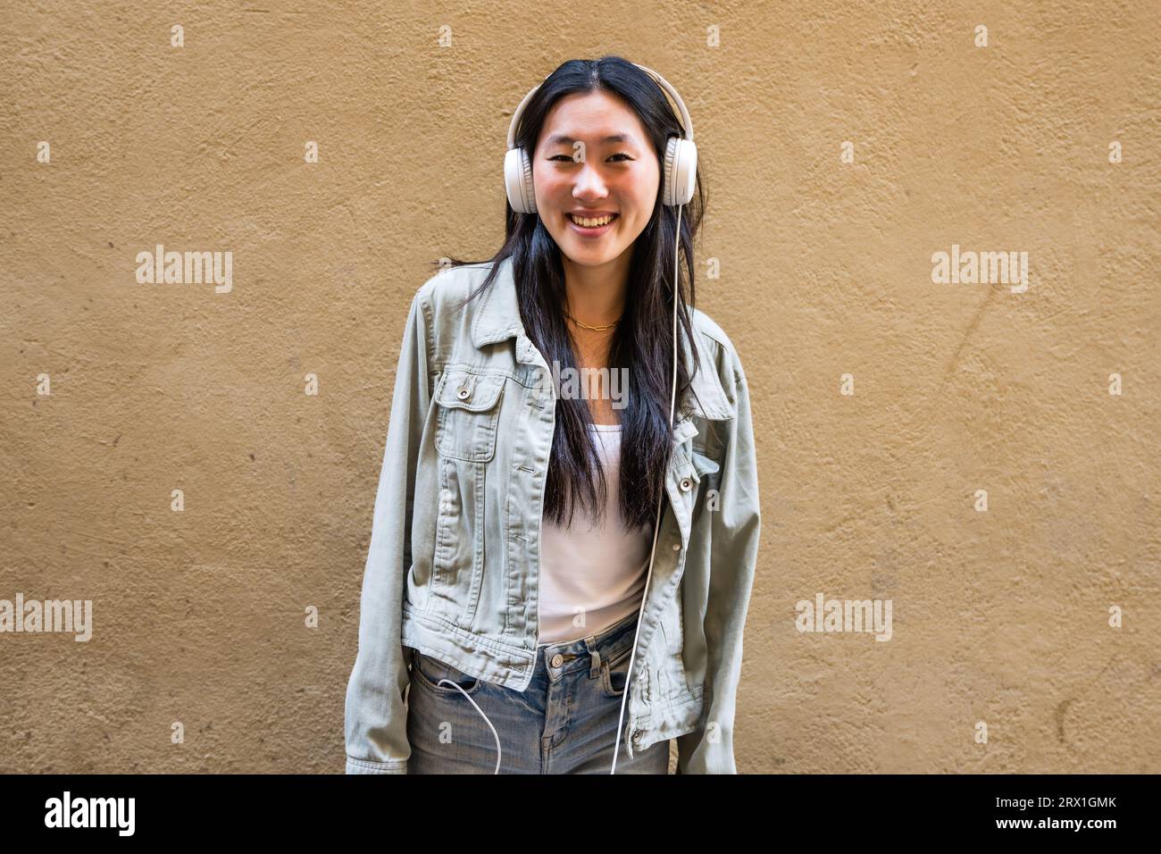 Fröhliches junges Mädchen, das draußen steht und Musik mit Kopfhörern hört Stockfoto