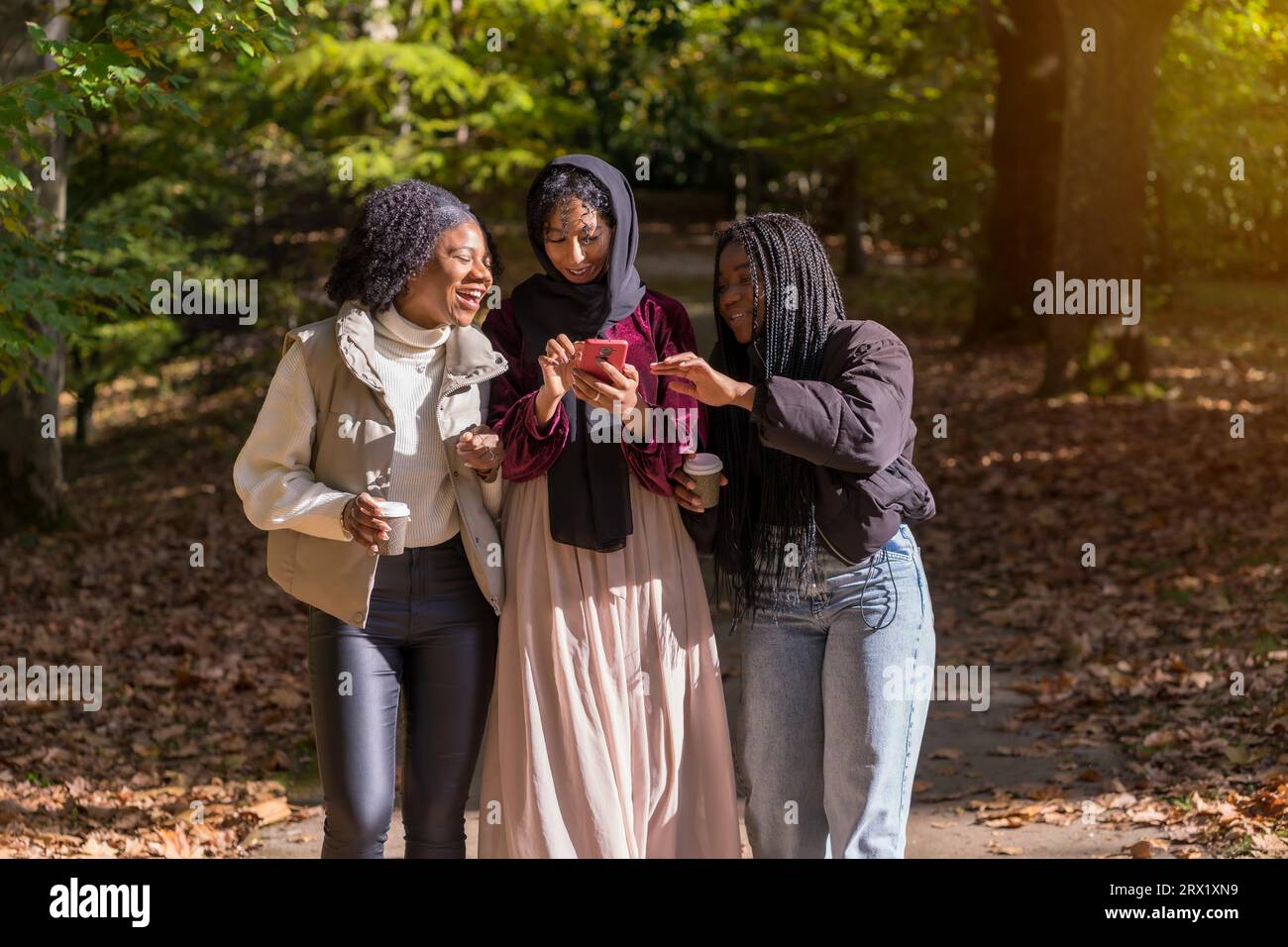 Multirassische Gruppe junger Frauen, die an einem sonnigen Tag mobil durch einen Park gehen Stockfoto