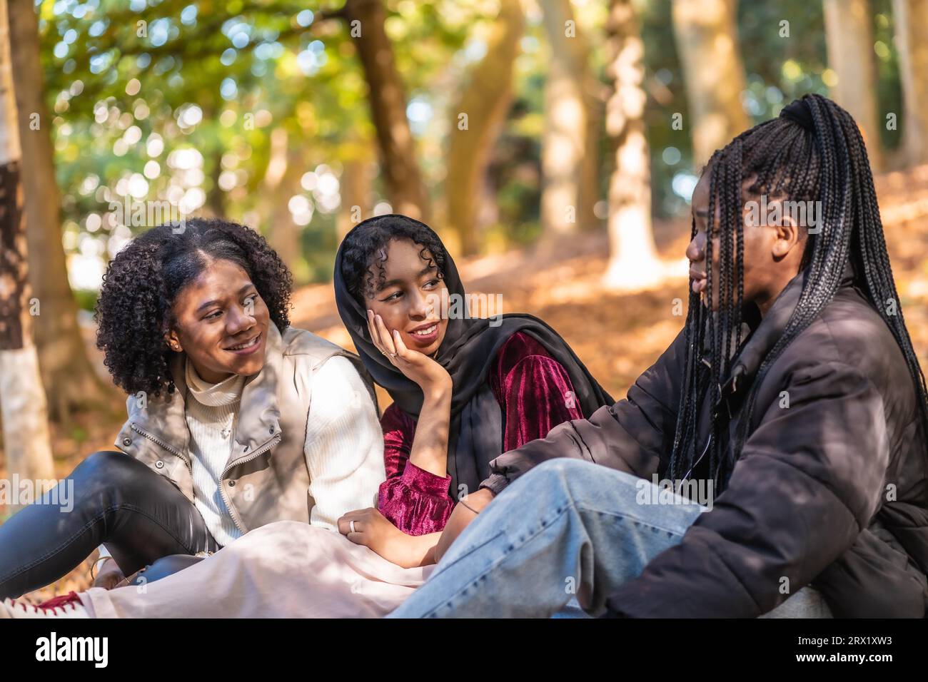 Gruppe von drei multikulturellen Freunden, die entspannt in einem Park sitzen Stockfoto