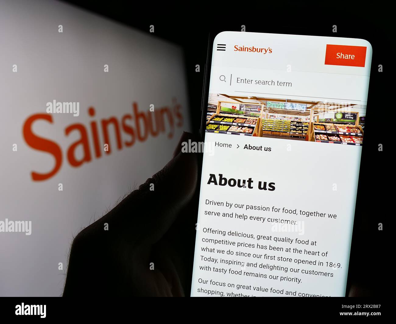 Person, die ein Mobiltelefon mit der Website des britischen Supermarktunternehmens J Sainsbury plc auf dem Bildschirm vor dem Logo hält. Konzentrieren Sie sich auf die Mitte der Telefonanzeige. Stockfoto