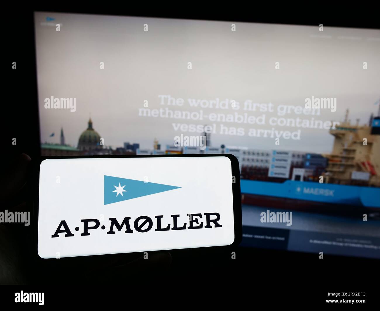 Person, die ein Smartphone mit dem Logo des dänischen Unternehmens A.P. Moller Holding AS (APMH) auf dem Bildschirm vor der Website hält. Konzentrieren Sie sich auf das Display des Telefons. Stockfoto