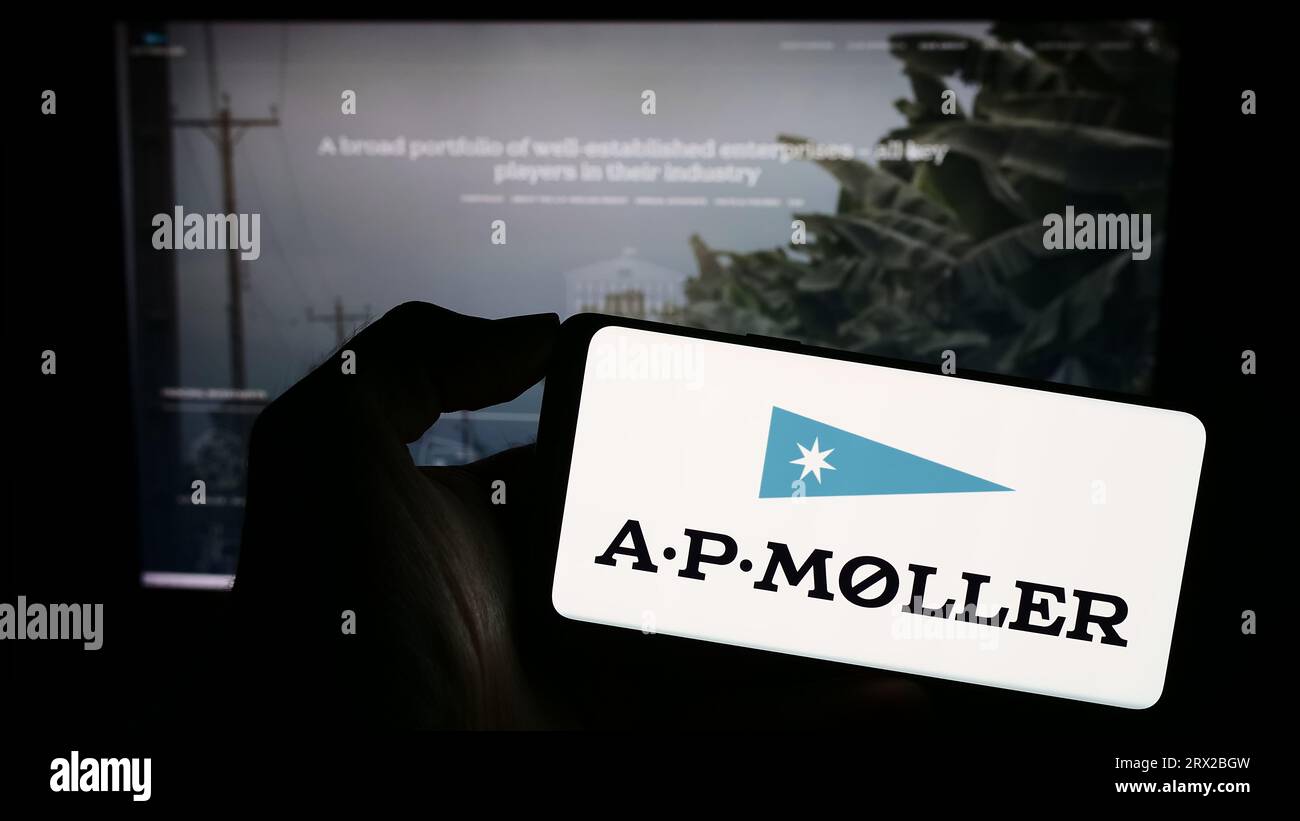 Person, die ein Mobiltelefon mit dem Logo des dänischen Unternehmens A.P. Moller Holding AS (APMH) auf dem Bildschirm vor der Webseite hält. Konzentrieren Sie sich auf das Display des Telefons. Stockfoto