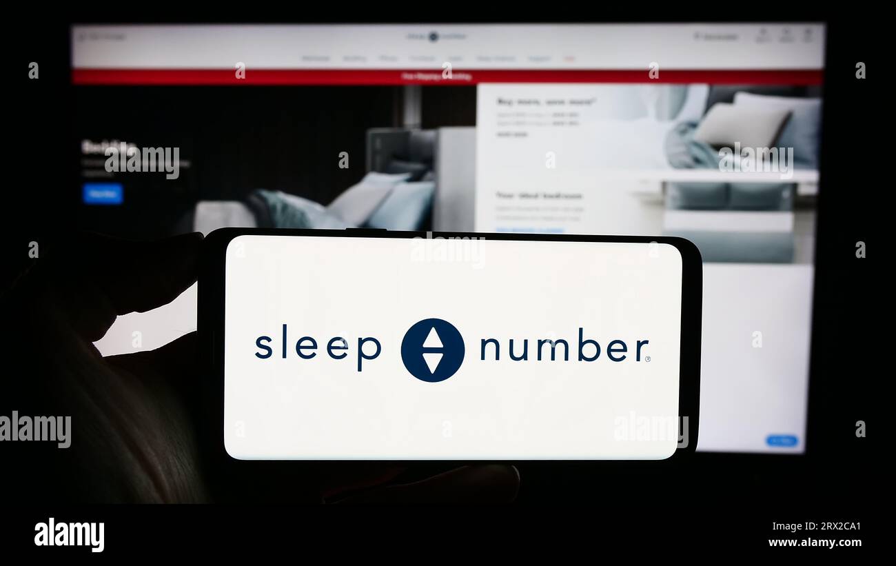 Person, die ein Smartphone mit dem Logo des US-amerikanischen Bettenunternehmens Sleep Number Corporation auf dem Bildschirm vor der Website hält. Konzentrieren Sie sich auf das Display des Telefons. Stockfoto