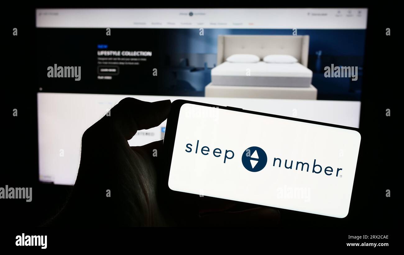 Person, die ein Mobiltelefon mit dem Logo des US-amerikanischen Bettenunternehmens Sleep Number Corporation auf dem Bildschirm vor der Business-Webseite hält. Konzentrieren Sie sich auf das Display des Telefons. Stockfoto
