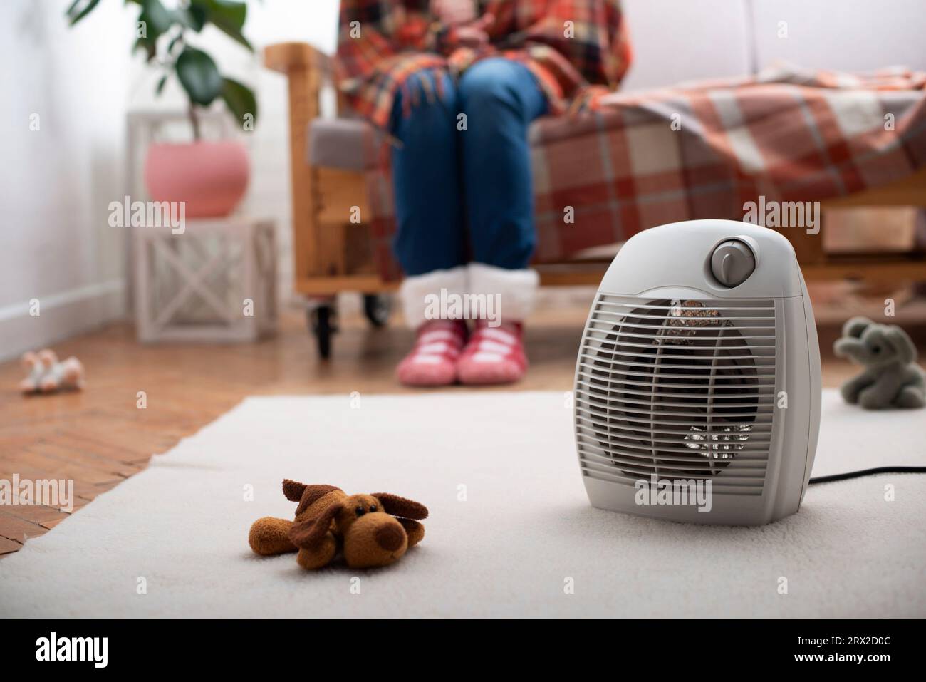 Elektrische Heizung mit Ventilator auf dem Boden im Wohnzimmer mit menschlichem Sitzen auf dem Sofa im Hintergrund Stockfoto