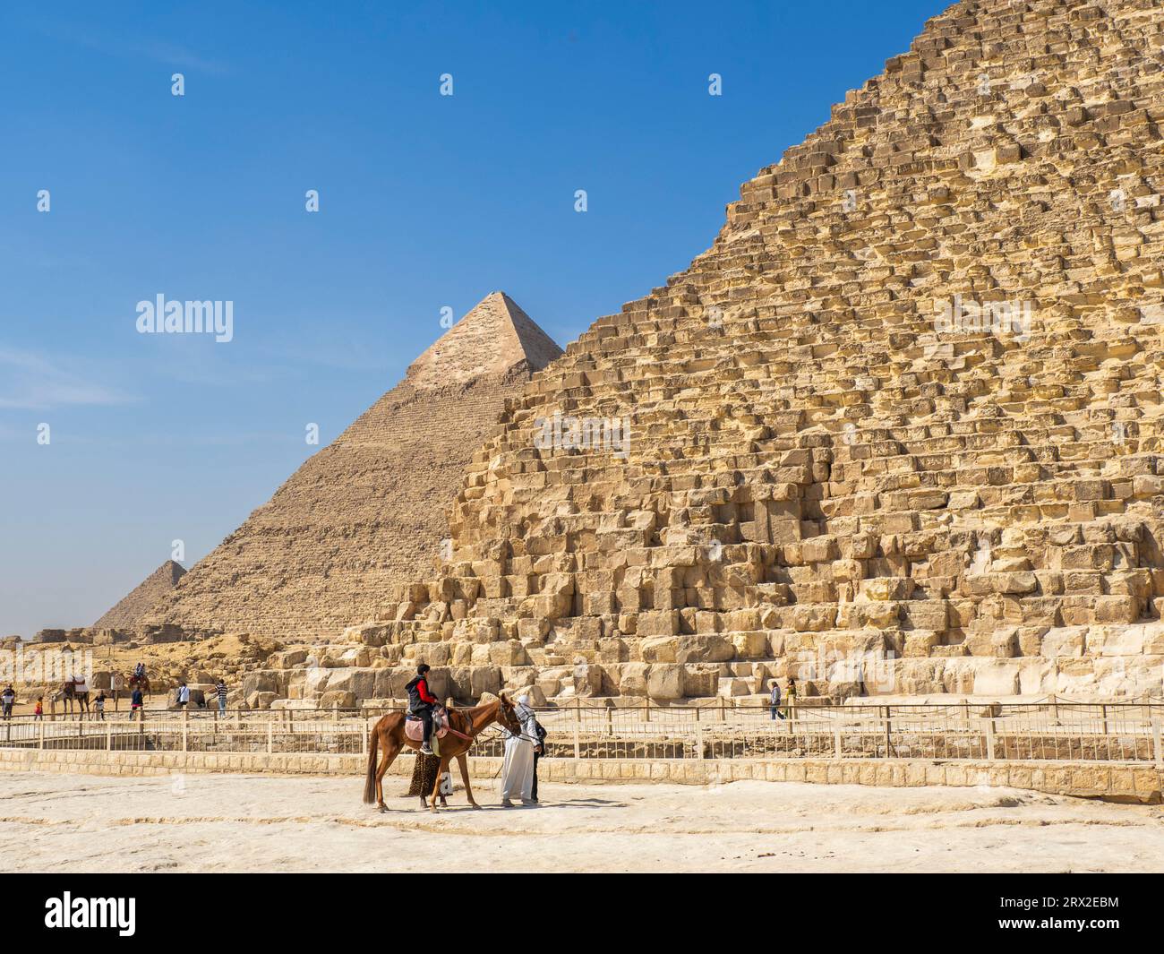 Touristen auf einem Kamelritt vor der Großen Pyramide von Gizeh, dem ältesten der sieben Weltwunder, Gizeh, in der Nähe von Kairo, Ägypten Stockfoto