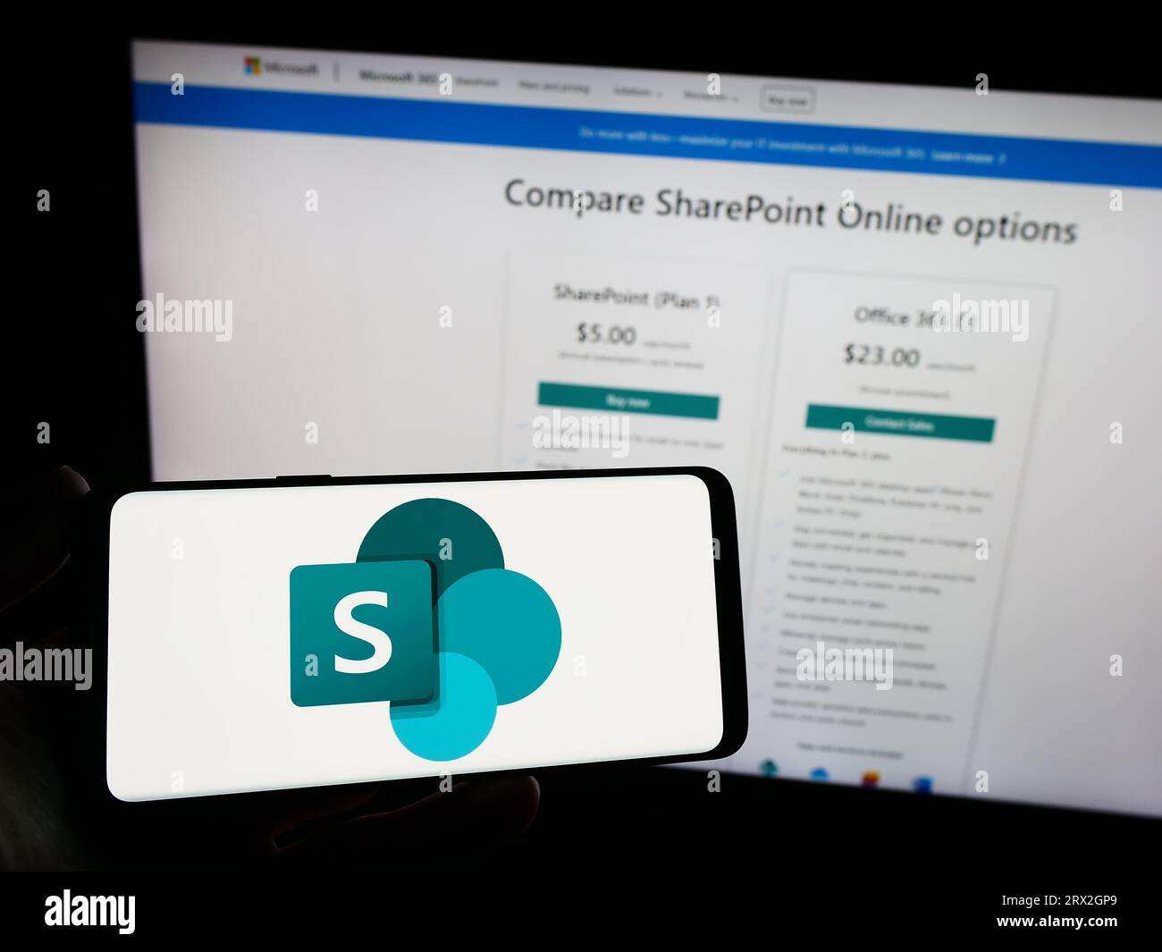 Person, die ein Mobiltelefon mit dem Logo der kollaborativen Plattform Microsoft SharePoint auf dem Bildschirm vor der Webseite hält. Konzentrieren Sie sich auf das Display des Telefons. Stockfoto