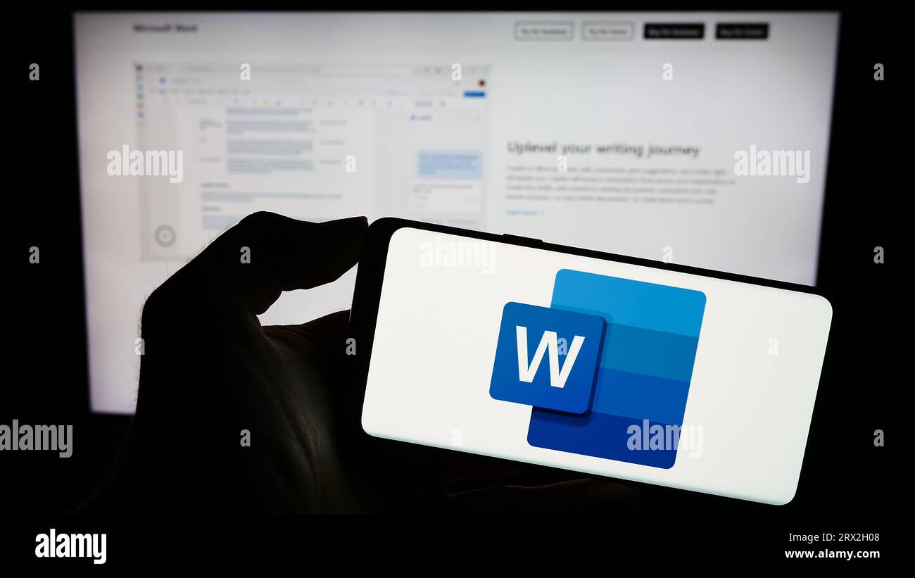 Person, die ein Mobiltelefon mit dem Logo der Textverarbeitungssoftware Microsoft Word auf dem Bildschirm vor der Geschäftswebseite hält. Konzentrieren Sie sich auf das Display des Telefons. Stockfoto