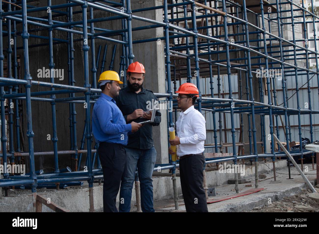 Ein Team von drei männlichen Bauingenieuren mit Schutzhelmen plant und diskutiert die nächste Bauphase auf der Baustelle. Stockfoto
