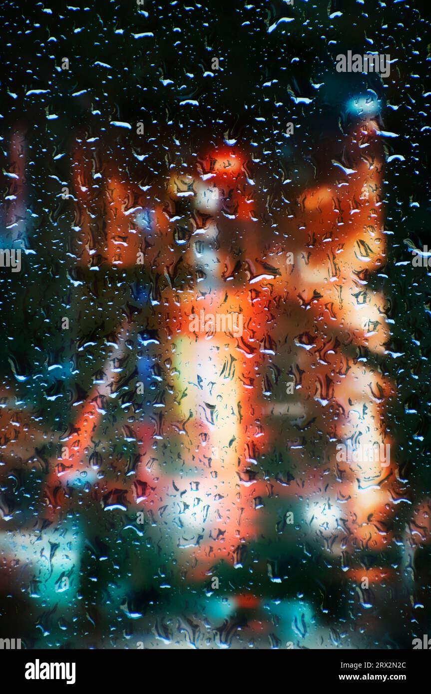 Fenster mit Regentropfen und verschwommener nächtlicher City-Szene dahinter Stockfoto
