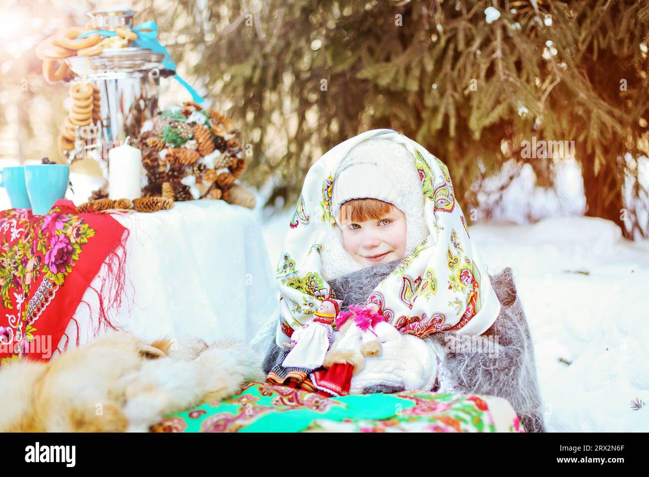 Ein süßes Mädchen in einem traditionellen russischen Kopftuch und Fäustlingen singt Volkslieder auf winterlichem Hintergrund. Nahaufnahme eines Kindes. Stockfoto