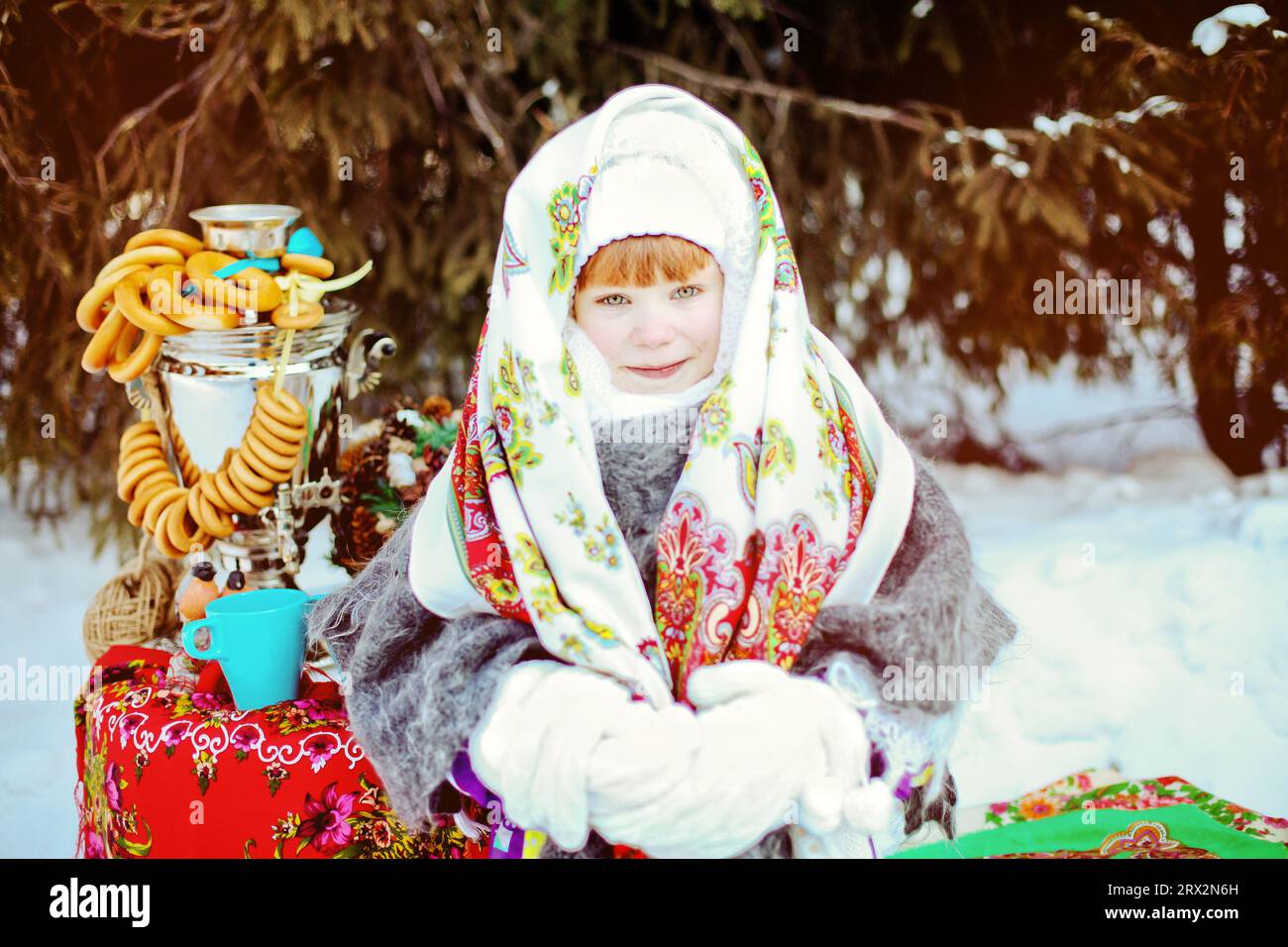 Ein süßes Mädchen in einem traditionellen russischen Kopftuch und Fäustlingen singt Volkslieder auf winterlichem Hintergrund. Nahaufnahme eines Kindes. Stockfoto