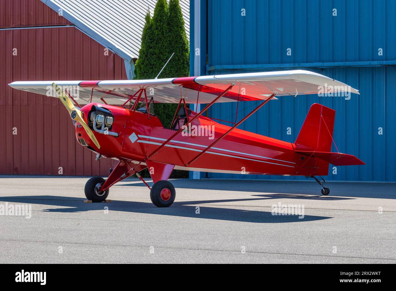 Ein kleines Flugzeug mit festen Flügeln steht vor zwei Hängern an einem Flughafen. Stockfoto