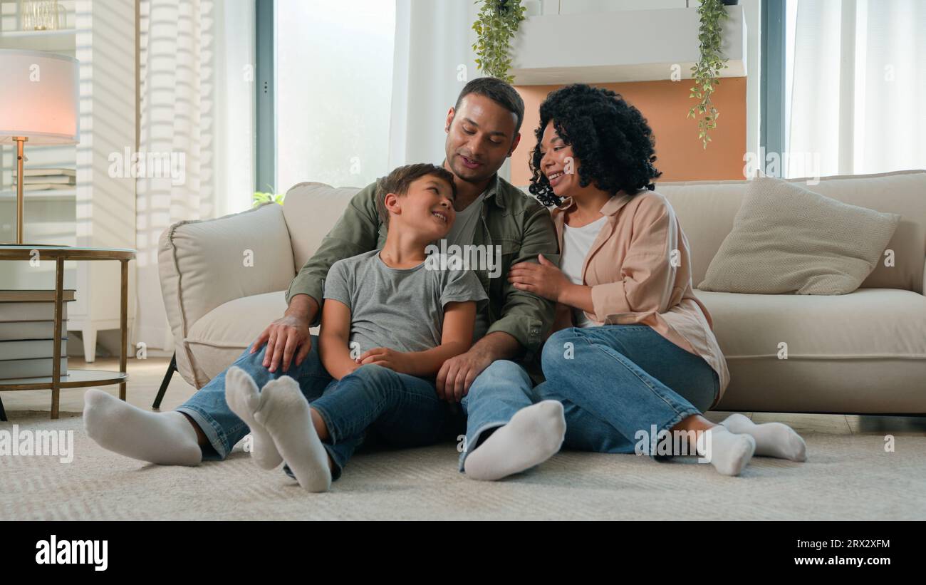 Multirassische glückliche Familie Wochenende afroamerikanische Mutter und Vater mit adoptierten Kaukasischen kleinen Jungen Kind Teen Kind Entspannen Sie sich auf dem Boden zu Hause Freizeit Stockfoto