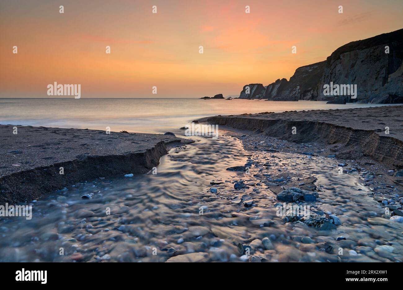Ein Bach durchschneidet den Sand, während er das Meer erreicht, in der Abenddämmerung, in Ayrmer Cove, einer abgelegenen Bucht in der Nähe von Kingsbridge, Südküste von Devon, England Stockfoto