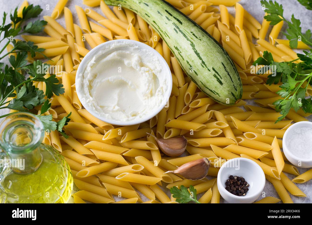 Lebensmittelhintergrund. Penne Pasta, Zucchini, Frischkäse, Olivenöl, Petersilie, Knoblauch, Salz und schwarzer Pfeffer, Draufsicht. Zutaten für die Zubereitung von vegetarischen p Stockfoto