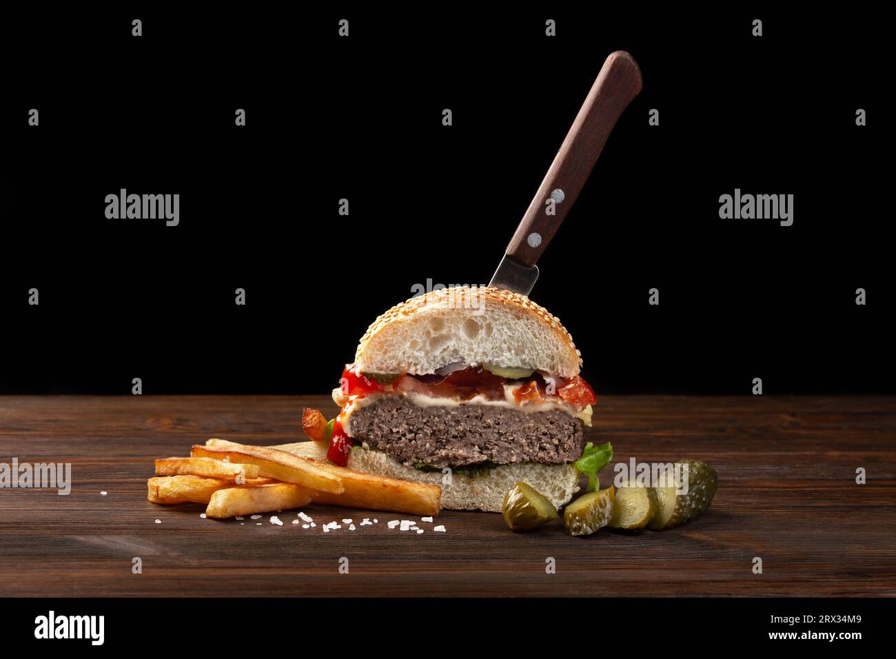 Hausgemachte Hamburger in der Hälfte close-up mit Rindfleisch, Tomaten, Salat, Käse und Pommes frites auf hölzernen Tisch. In der Burger stecken ein Messer. Fastfood auf Stockfoto