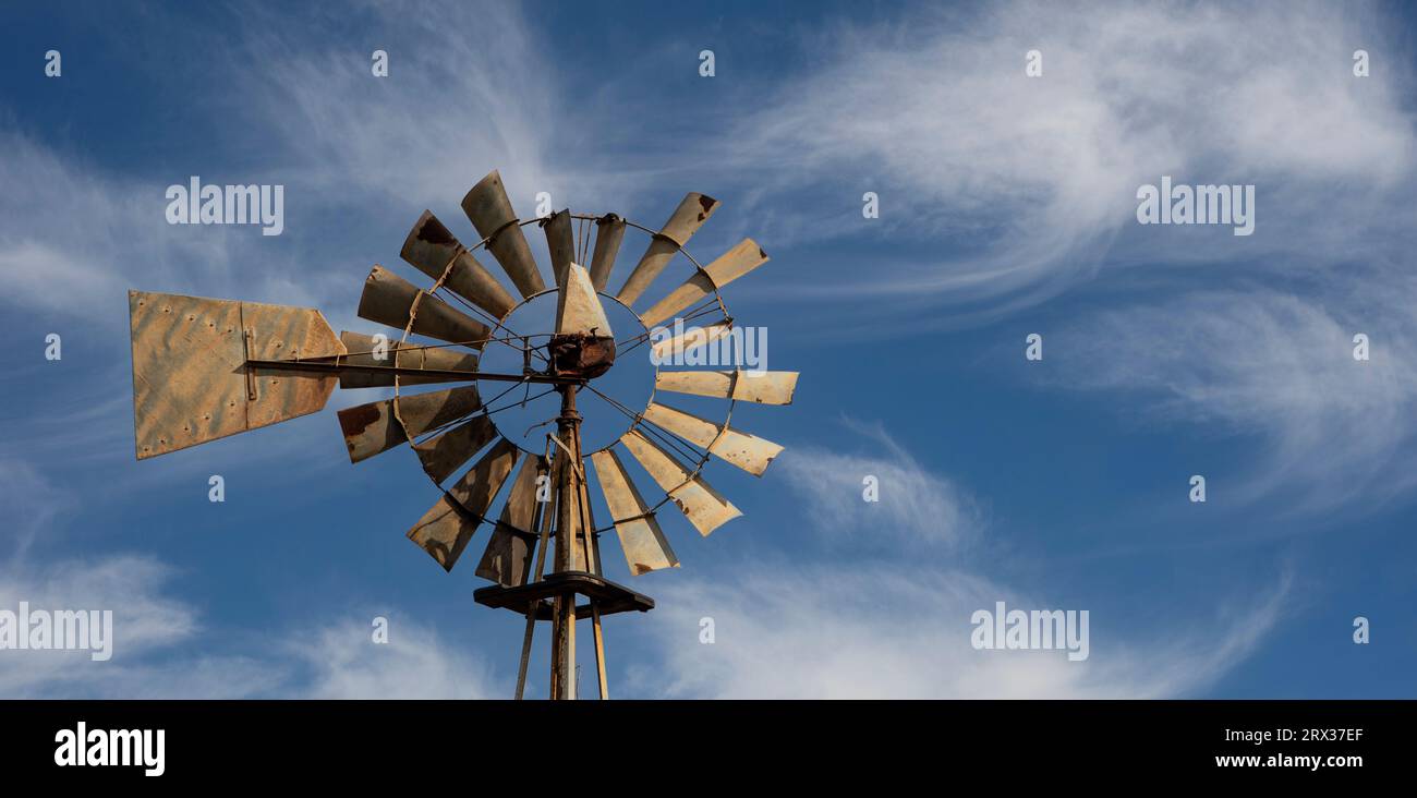 Altmodische, mehrflügelige Windpumpe aus Metall auf einem Turm vor einem blauen Himmel. Stockfoto