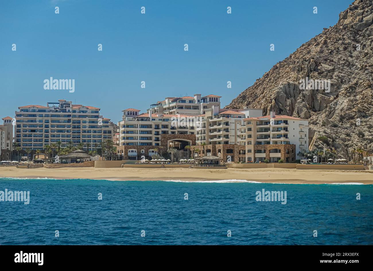 Mexiko, Cabo San Lucas - 16. Juli 2023: Grand Solmar Lands End Resort und Spa-Gebäude hinter Sandstrand und Surfen von blauem Wasser unter blauem Himmel Stockfoto