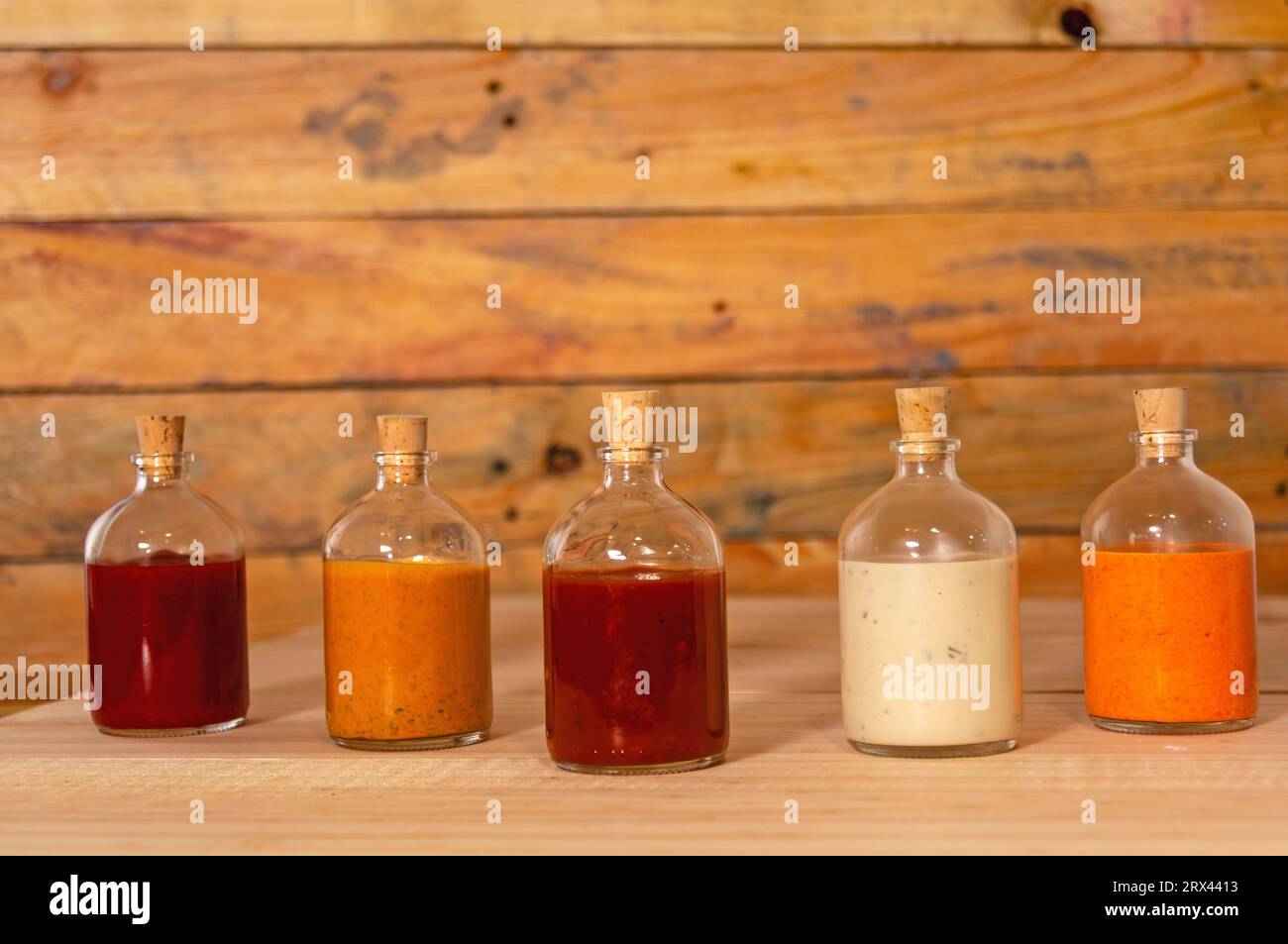Handgemachte scharfe Saucen in Glasflaschen mit Kork auf farbigem Holzsockel - Salsas picantes hechas artesanalmente en botellas de vidrio con corcho Sob Stockfoto