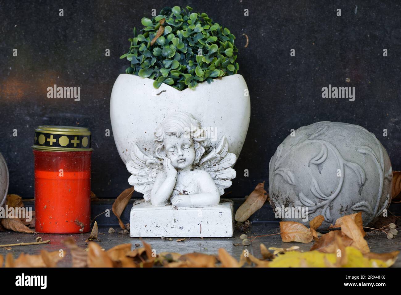 Herbstlaub liegt auf einer Grabdekoration mit Grablicht und einer Blumenvase mit Engelsfigur Stockfoto