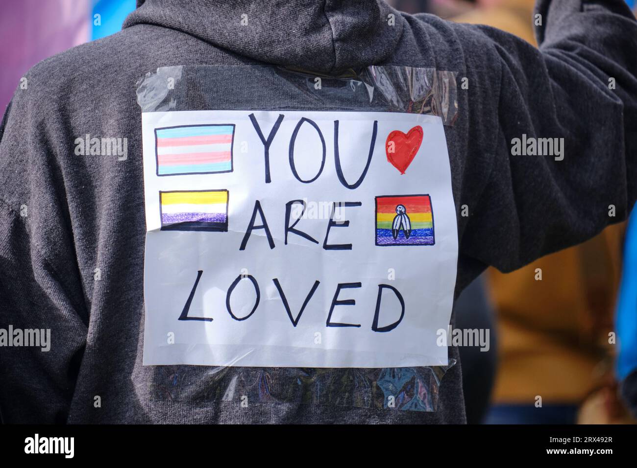 Handgezeichnetes Schild: „You are loved“ auf der Rückseite des Pro LGBTQ+-Gegenprotestiers bei der Anti-Trans-Rallye Stockfoto
