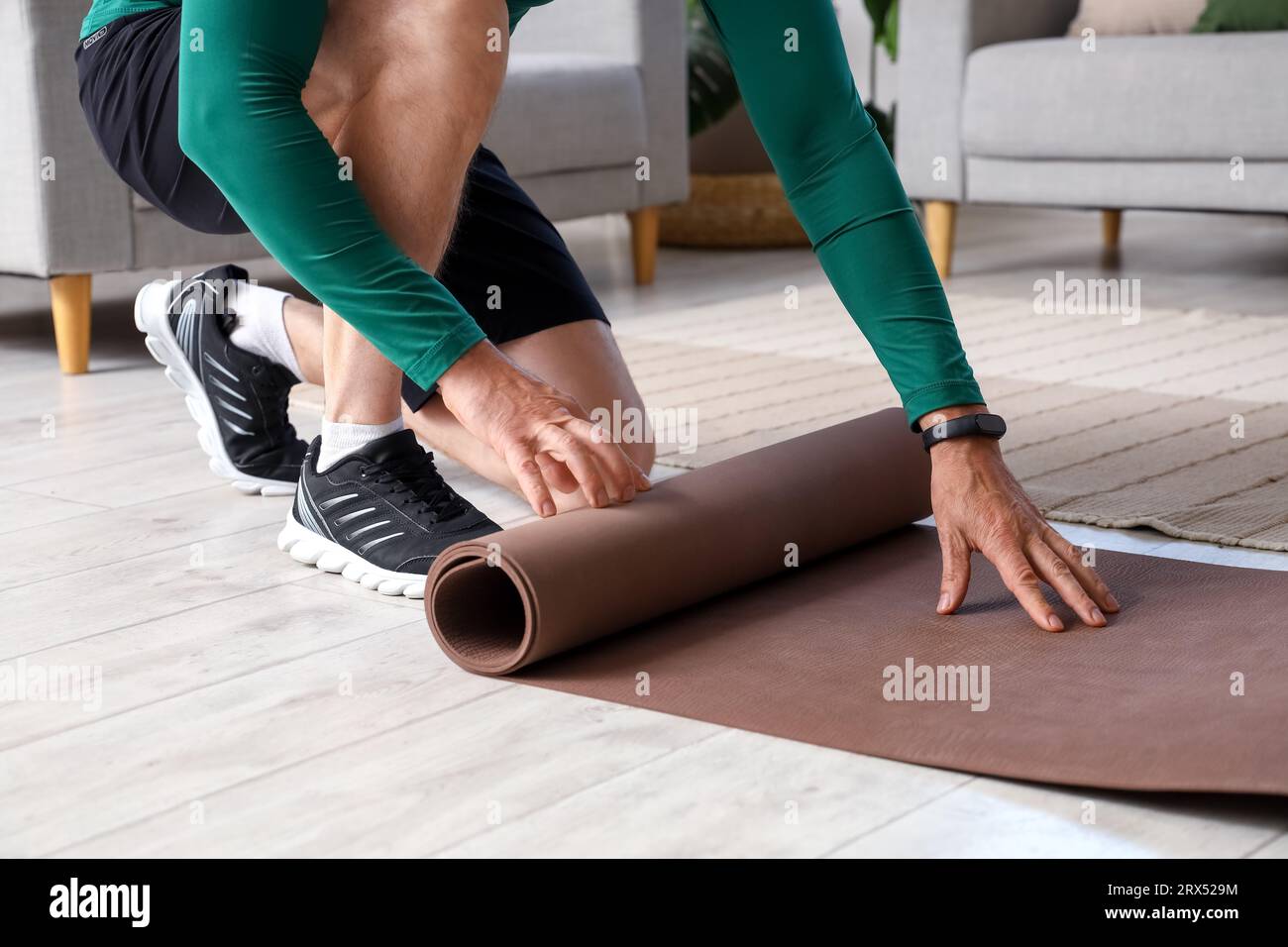 Sportlicher Reifer Mann, der sich zu Hause die Fitnessmatte ausrollen lässt, Nahaufnahme Stockfoto