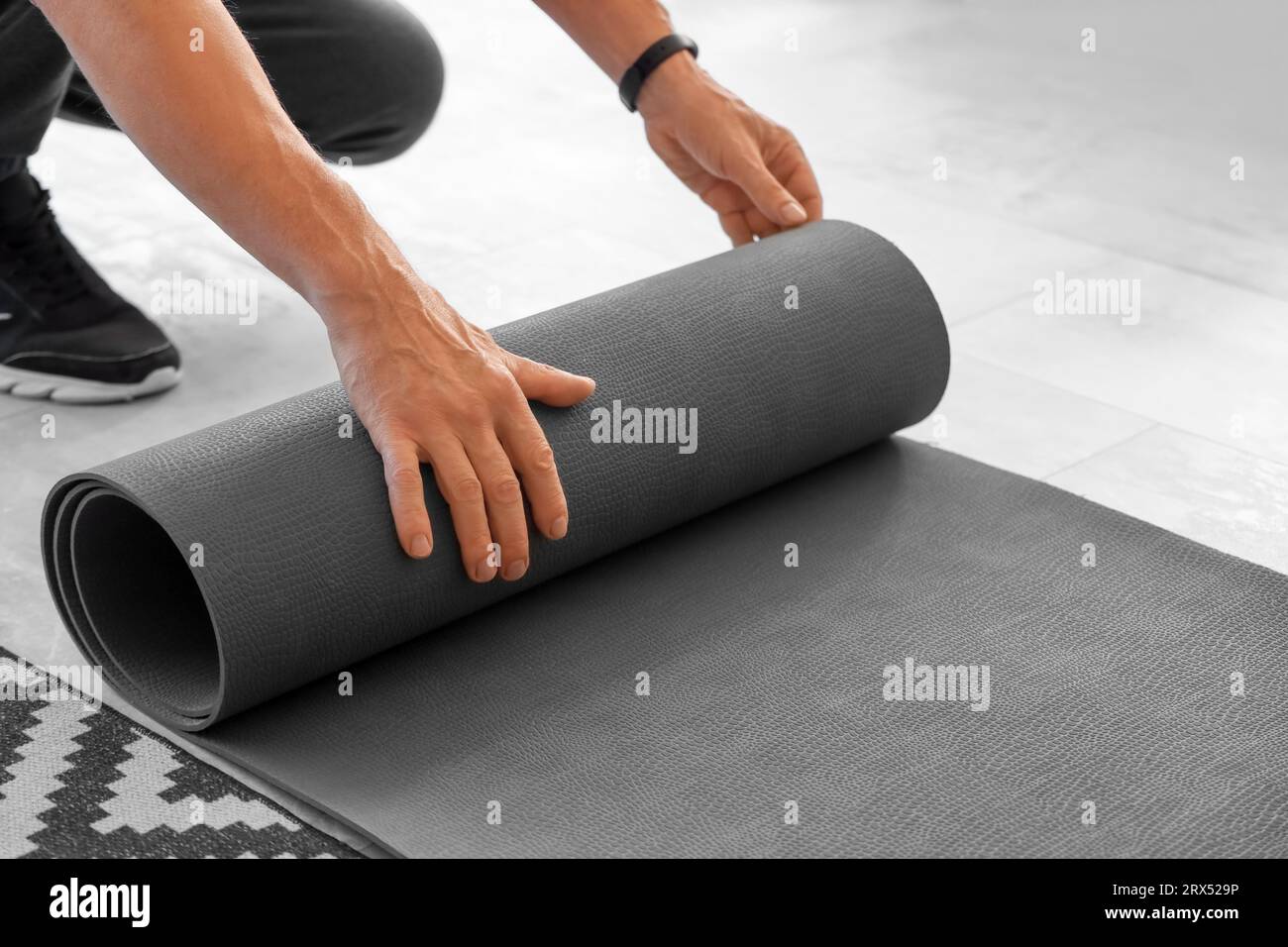 Sportlicher Reifer Mann, der sich zu Hause die Fitnessmatte ausrollen lässt, Nahaufnahme Stockfoto