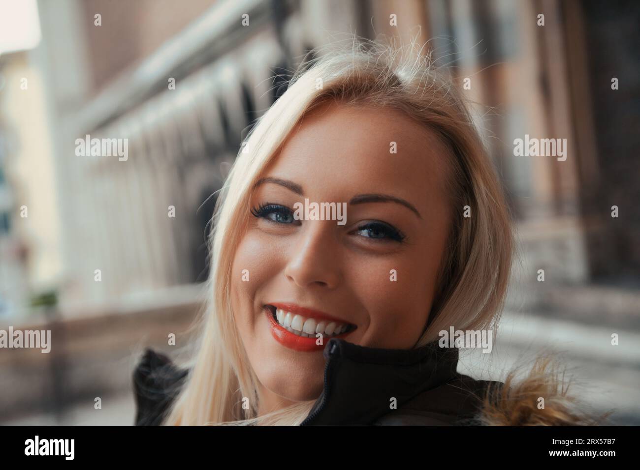 Das strahlende Lächeln und das makellose Make-up der jungen blonden Frau füllen den Rahmen, während sie ihre europäische Reise genießt. Dank des kulturellen Austauschs der Studenten Stockfoto