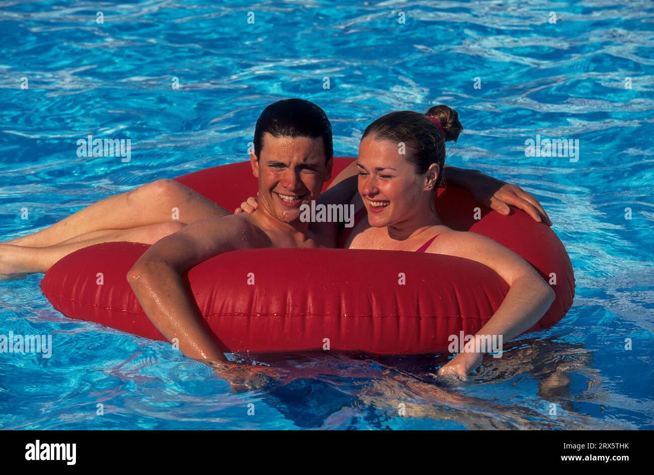 Junges Paar, das mit rotem schwimmendem Reifen im Swimmingpool herumtobt Stockfoto