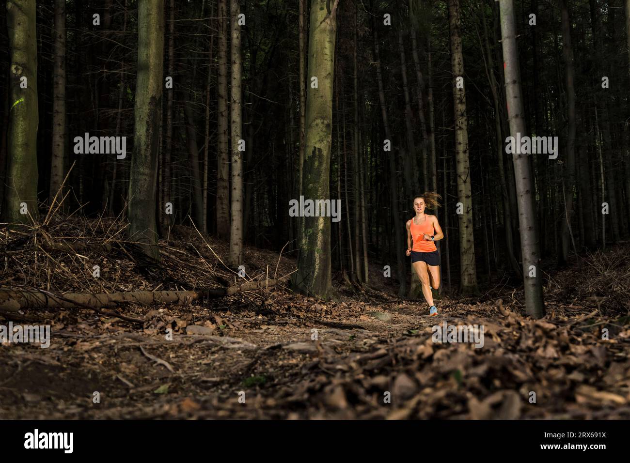 Engagierte Sportlerin, die im Wald zwischen Baumstämmen läuft Stockfoto